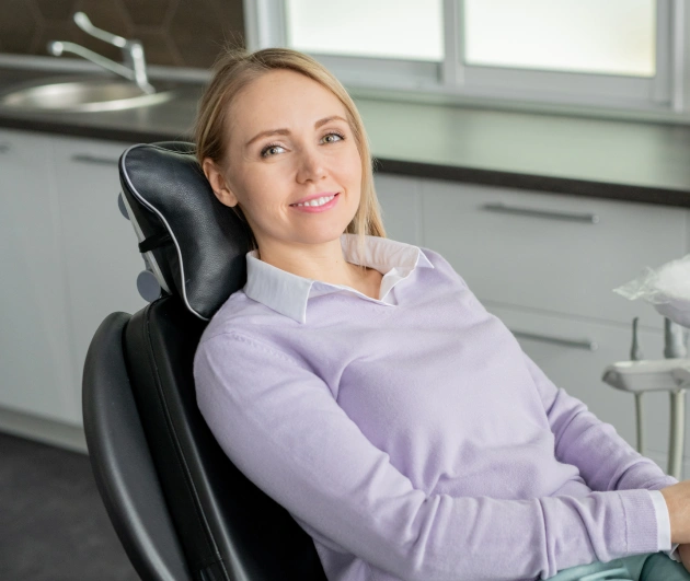 Woman in lavender sweater reclines in dental chair at modern dental office.