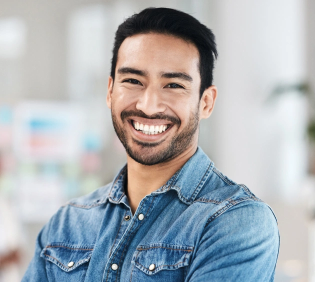 Smiling male dental professional in denim shirt at modern dental office setting.
