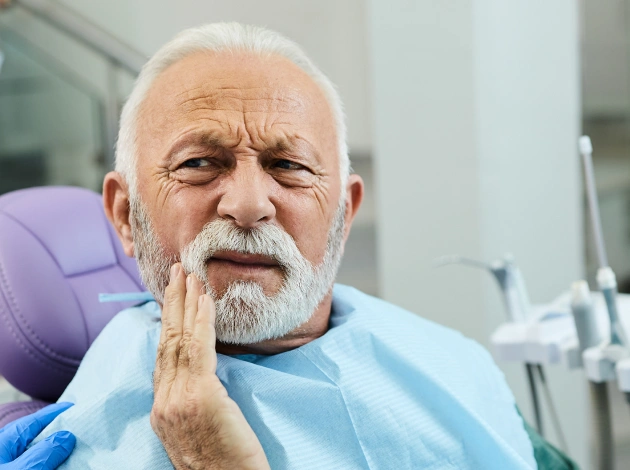 Older man with beard touching jaw in pain, seated in dental chair at clinic