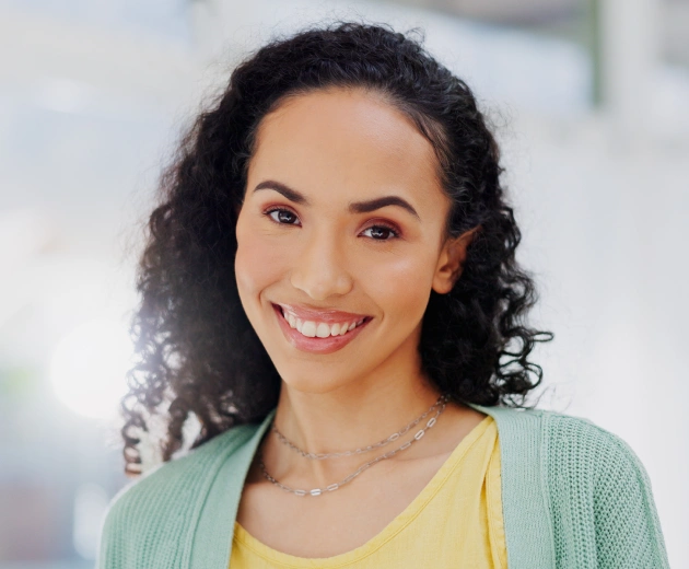 Smiling woman in yellow shirt and green cardigan in bright dental office setting.