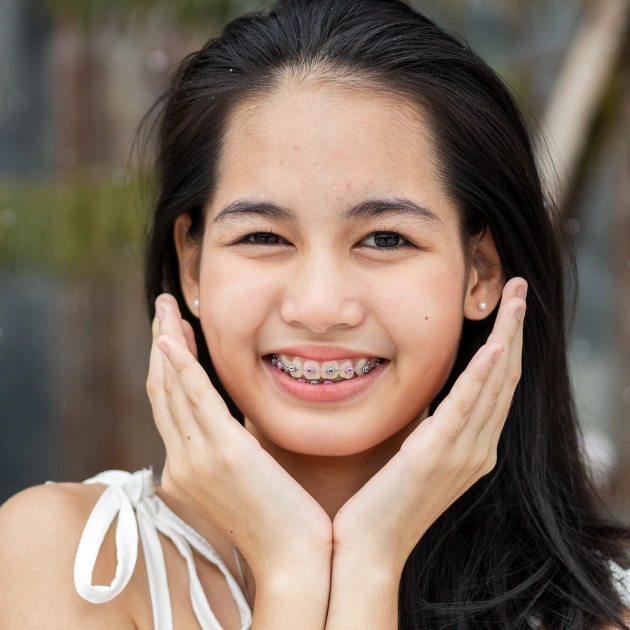 Young girl smiling with braces, hands to face, outdoor portrait for dental care website.