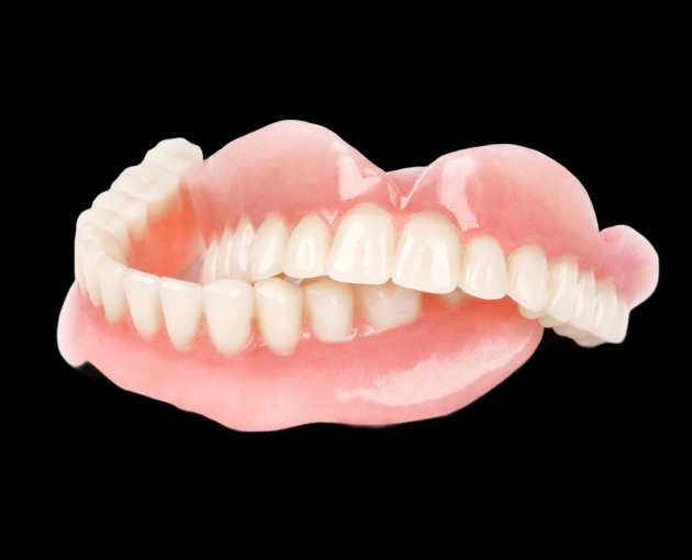Dentures showing upper and lower false teeth with pink gums on black background.