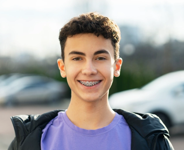 Smiling teenage boy wearing purple shirt outdoors with parked cars in background