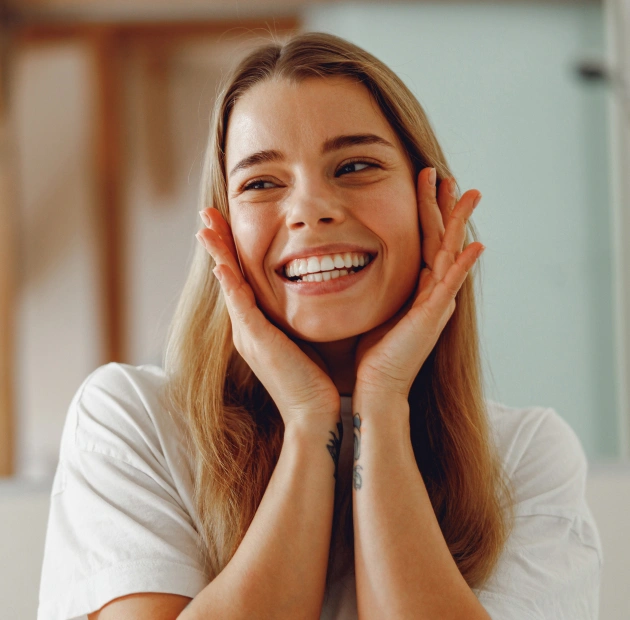 Happy woman smiling with hands to face in bright dental office setting.