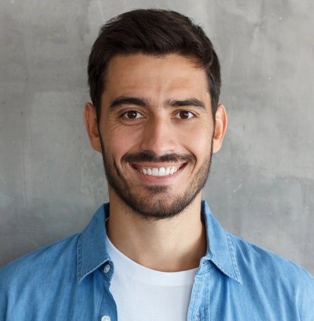 Professional headshot of smiling male staff member wearing blue shirt against gray background.
