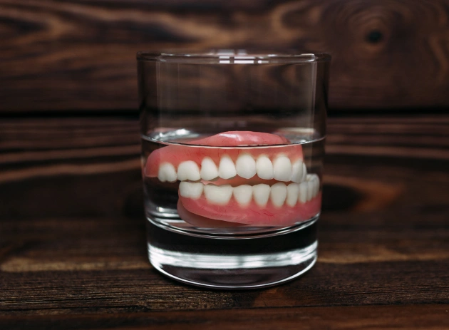 Dental prosthetic teeth model displayed in glass of water on wooden surface
