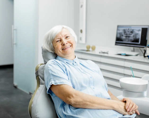 Senior woman smiling in dental office chair during examination or consultation visit.