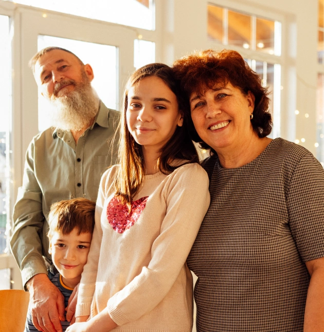 Multi-generational family smiling together indoors near bright windows at dental care facility.