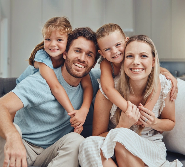 Happy family of four smiling together indoors in casual clothing.