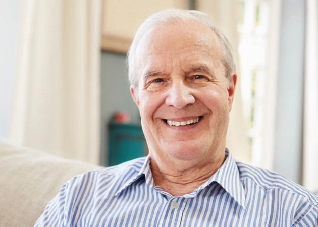 Smiling older man in striped shirt sitting indoors, dental care professional portrait.