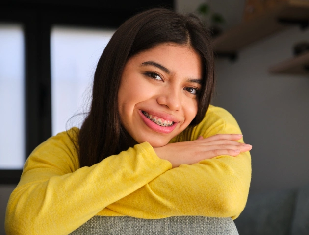 Smiling woman in yellow shirt resting on chair in modern dental office setting.