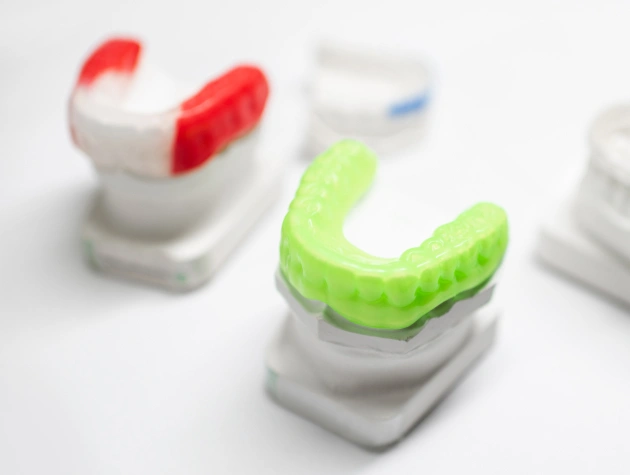 Colorful dental retainers and mouth guards displayed on white stands showcasing orthodontic appliances.