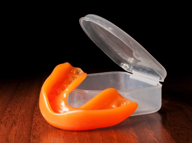 Orange bell pepper slices in clear plastic container on wooden surface, dark background.