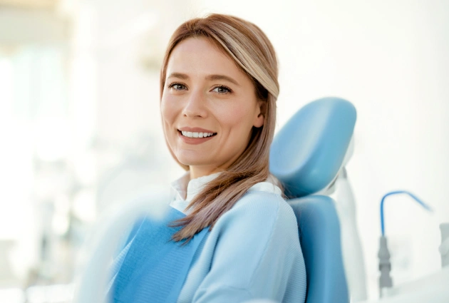 Smiling female dental professional in blue scrubs seated in dental chair at practice.