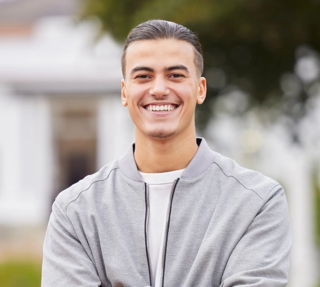 Young man smiling outdoors in casual gray jacket, dental care professional portrait.