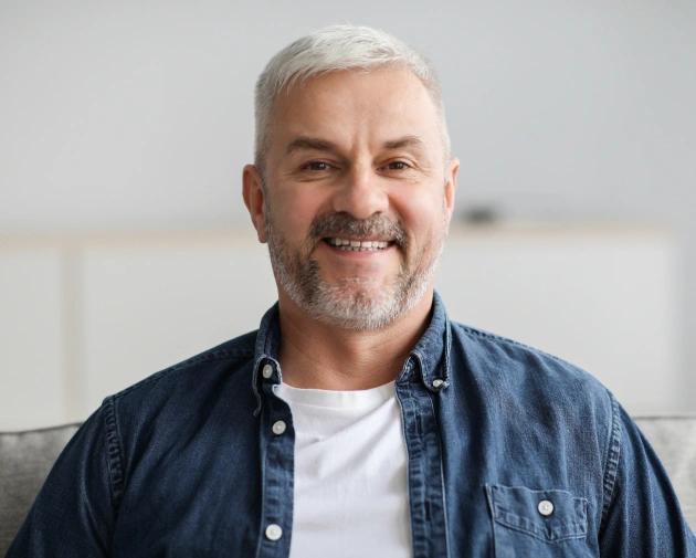Smiling middle-aged man with gray hair wearing blue shirt in dental office setting.