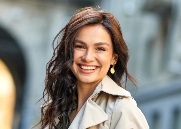 Woman smiling at camera wearing light-colored shirt, professional dental office setting.