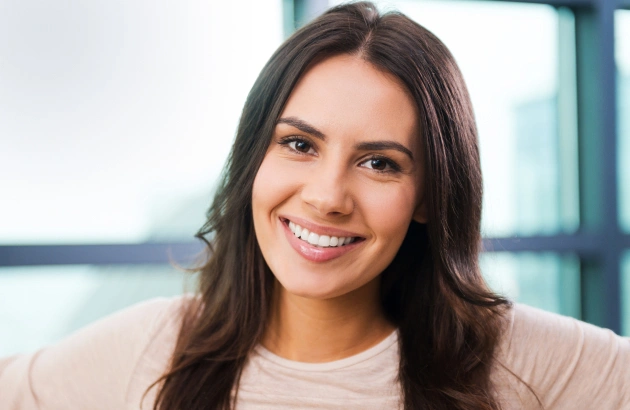 Smiling female dental professional in modern clinic with large windows and contemporary interior design.