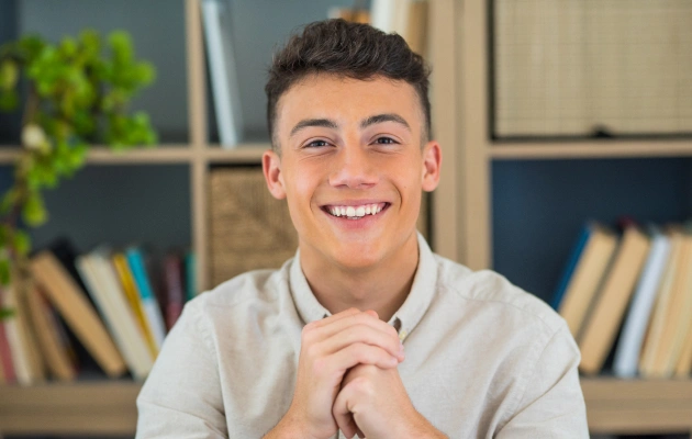 Young male dentist smiling at camera in modern dental office with bookshelf background