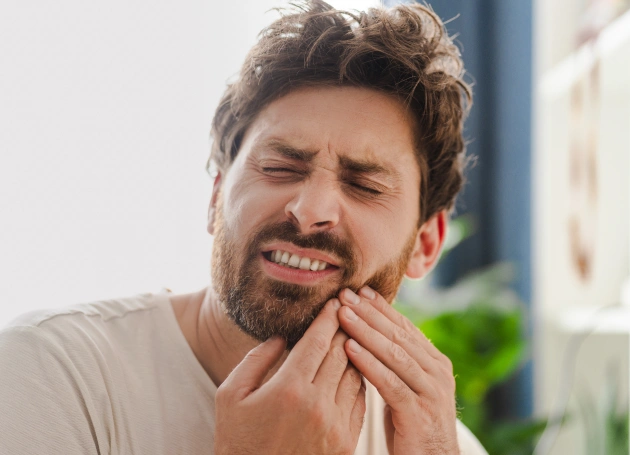 Man holding cheek in pain, experiencing dental discomfort indoors
