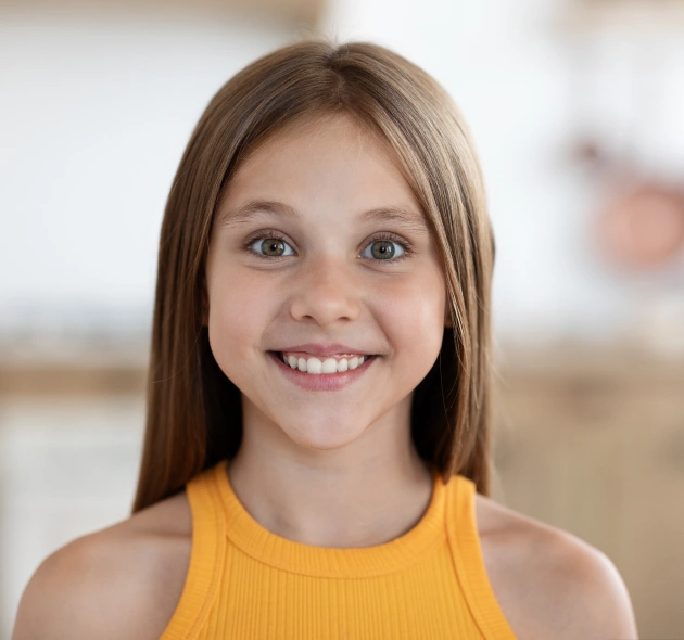 Smiling young girl in yellow tank top, indoor setting, dental care website portrait.