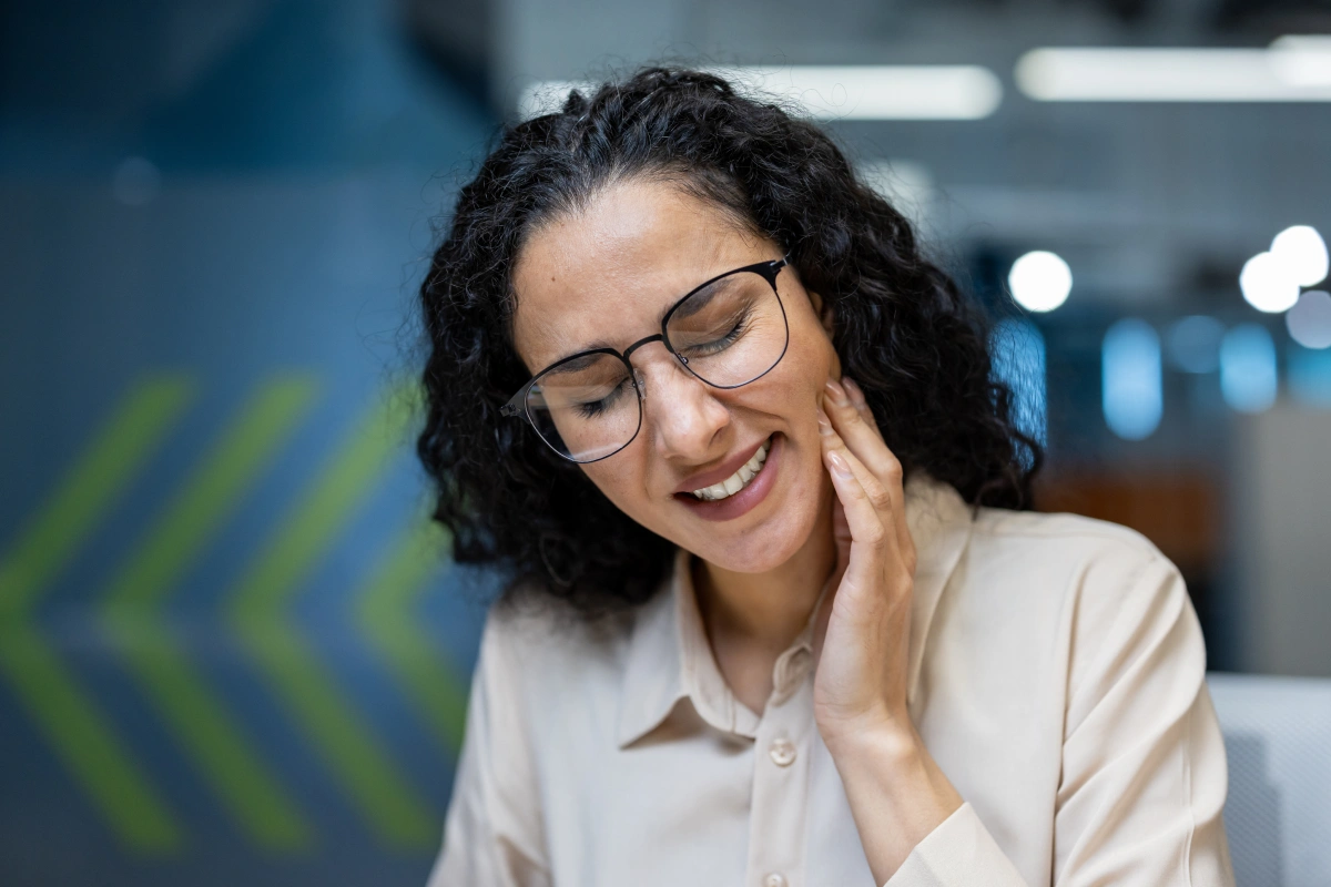 Smiling woman with glasses wearing white coat in modern dental office setting.