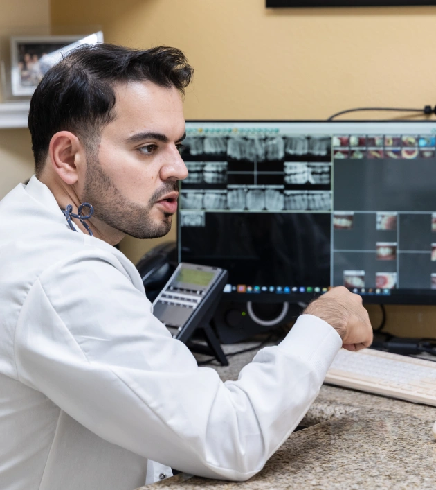 Dentist reviewing digital dental imaging on computer monitors in clinical office setting.