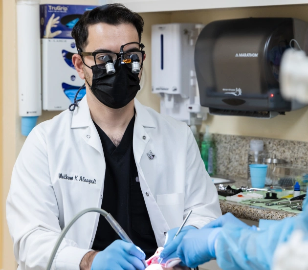 Male dentist in white coat and mask working in dental clinic treatment room.